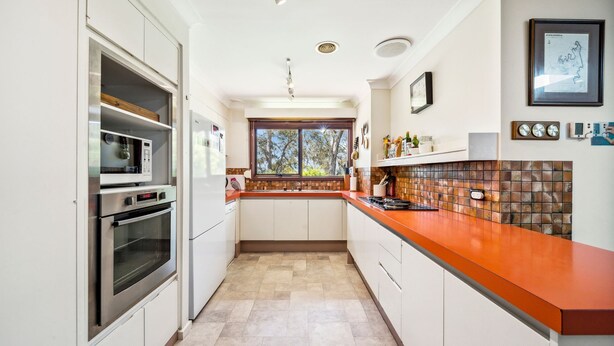 A modern kitchen with white cabinetry, a red countertop, and a window providing natural light. - Rosella Retreat | Perfect getaway for family and friends (Blackheath)
