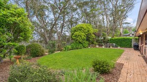 A well-maintained backyard with a lawn, various shrubs, and a patio area with outdoor furniture. - Rosella Retreat | Perfect getaway for family and friends (Blackheath)