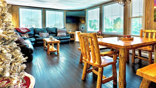 A spacious living room with a large sectional sofa, a wooden dining table with chairs, and a Christmas tree. - North Pole Christmas, Michigan Spectacular Lake Superior, Grand Island View! (Christmas)