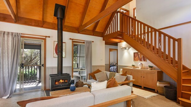 Una sala acogedora con chimenea, escalera de madera y vistas al exterior.
