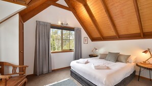 Un dormitorio con una cama grande, un banco de madera, una ventana con cortinas y un techo con vigas a la vista.