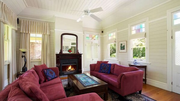 A living room with a fireplace, two red sofas, a coffee table, and a ceiling fan.