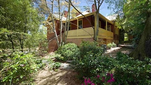 Un chalet rustique doté d’un porche en bois, entouré d’une végétation luxuriante et de plantes en fleurs.