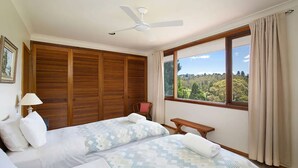 Ein Schlafzimmer mit zwei Betten, einem Deckenventilator, einem Fenster mit Blick auf einen Wald und einem Holzschrank.