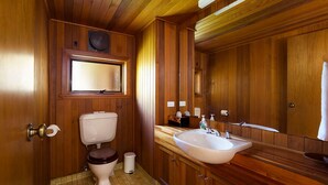 Ein Badezimmer mit Holzwandverkleidung, ausgestattet mit Toilette, Waschbecken, Spiegel und einem Fenster über der Toilette.