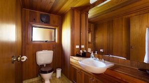 A wooden-paneled bathroom with a toilet, sink, mirror, and a window above the toilet. - Stableford Lodge | Overlooking Golf Course | open fireplace (Blackheath)