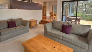 Een moderne woonkamer met twee grijze banken, een houten salontafel, en een eethoek met een houten tafel en stoelen.
