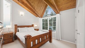 Ein Schlafzimmer mit einem hölzernen Bett, zwei Nachttischen, einem Schranken und einem Fenster mit Vorhängen sowie einer Tür.