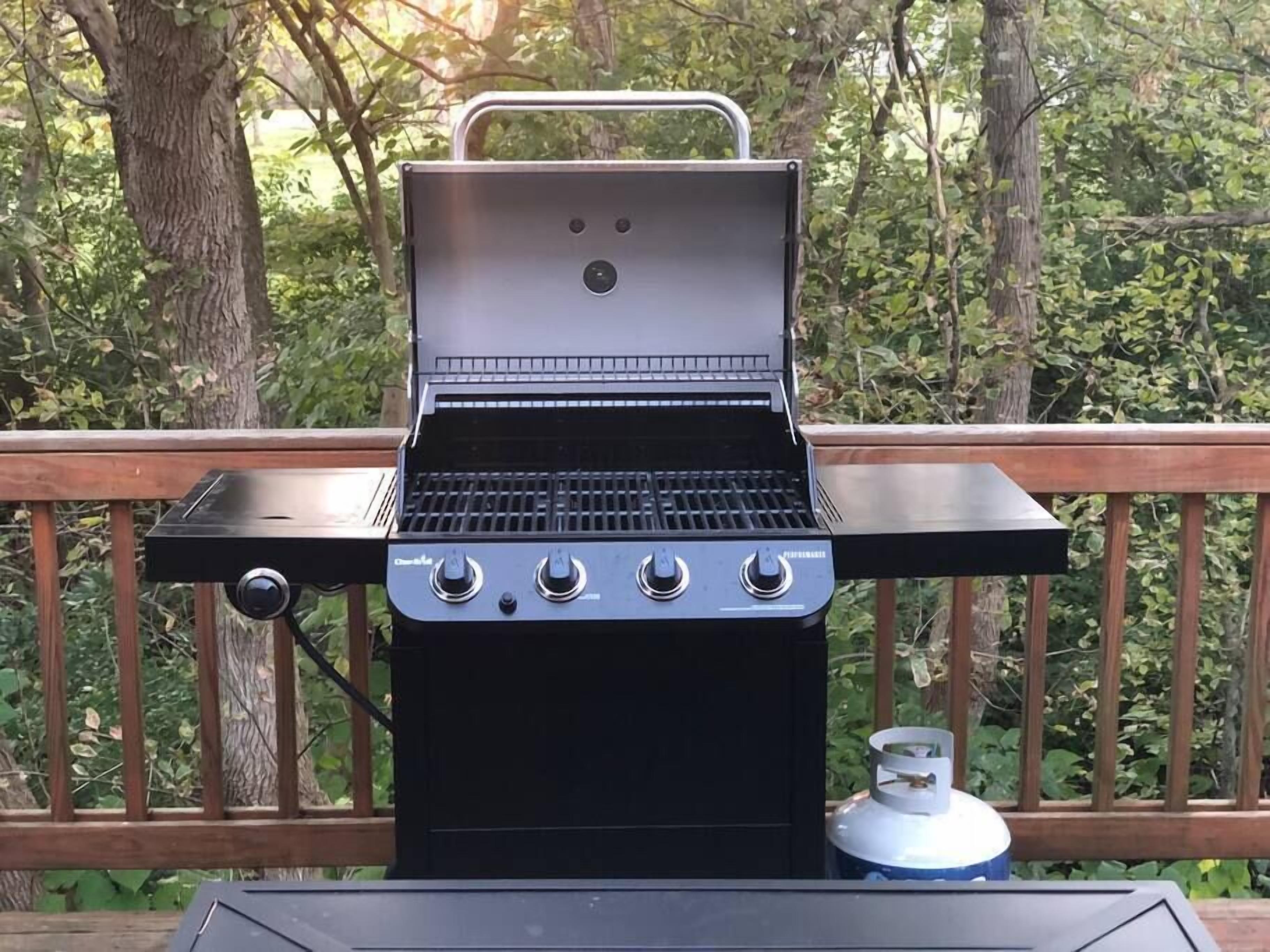 Un barbecue au gaz portatif doté de quatre boutons de contrôle, d’un écran numérique et d’une bouteille de gaz, le tout posé sur une terrasse en bois.