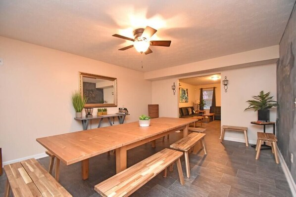 A spacious dining area with a long wooden table and benches, a ceiling fan, and a mirror on the wall.