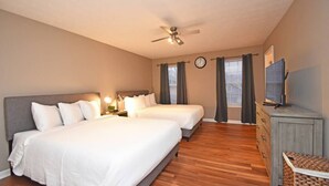 A bedroom with two beds, a ceiling fan, a clock, a television, and a wooden dresser. - Kings Manor · The Best of North Cincinnati @ Kings Manor (Kings Mills)