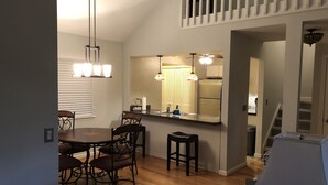 A dining area with a wooden table and chairs, a kitchen with a refrigerator and sink, and a staircase leading to an upper level. - Keowee Key Townhome - Pet Friendly, View of Golf Course plus Amenities (Salem)