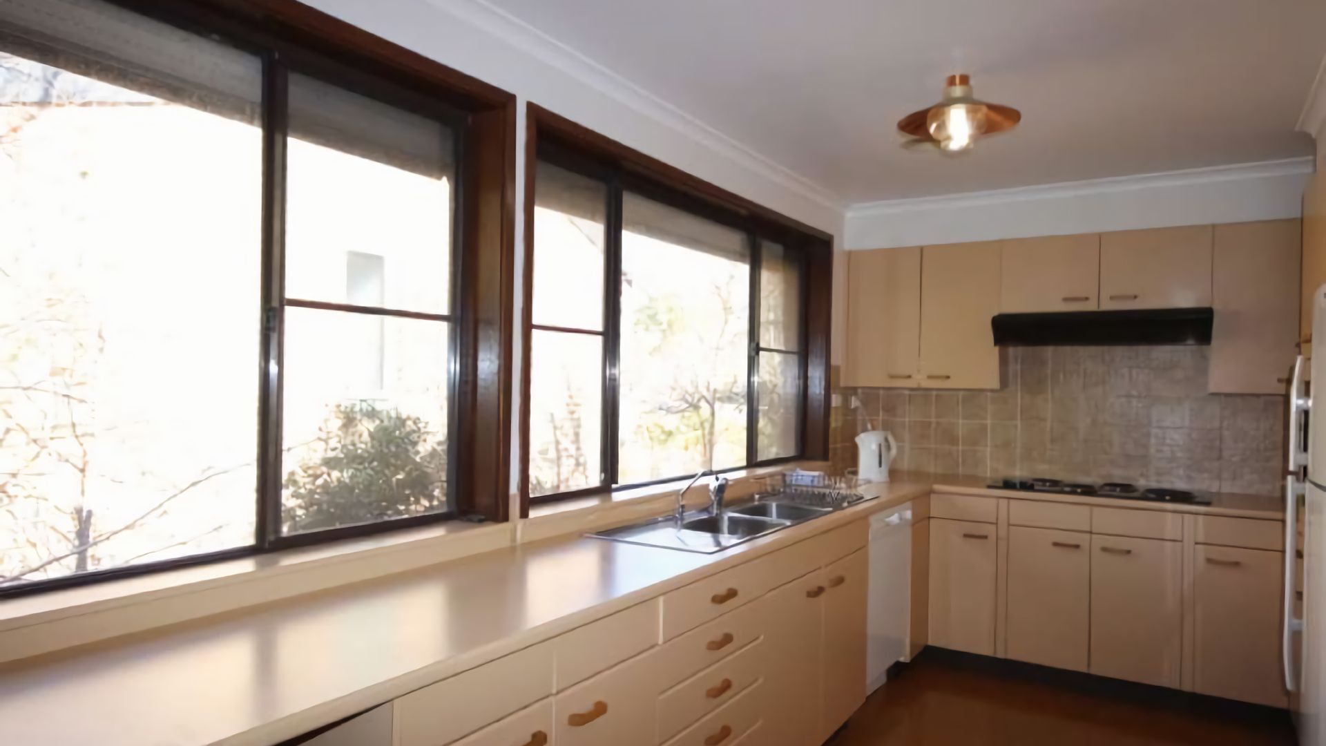 A kitchen with a large window, a sink, cabinets, and a stove.