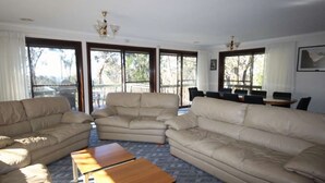 Un salón espacioso con sofás color beige, una mesa de centro de madera y grandes ventanales con vistas al exterior.
