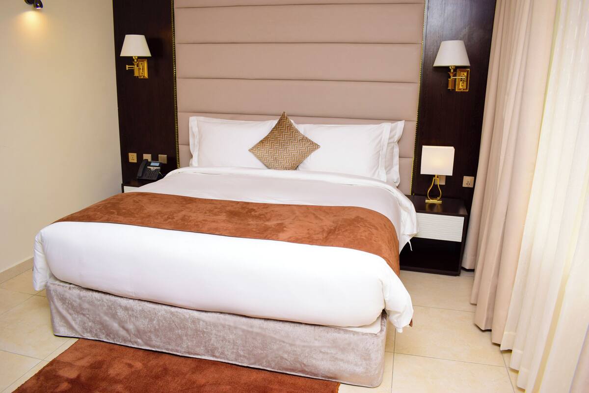 Quarto de hotel com cama grande, duas luminárias laterais, mesa de cabeceira e telefone.