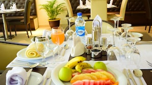 A dining table set with a variety of fruits, a bottle of water, and multiple wine glasses. - Monty Suites & Golf (Uyo)