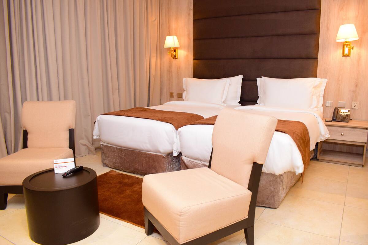 Quarto de hotel com uma cama grande, duas poltronas, uma mesinha redonda e um telefone na mesinha de cabeceira.