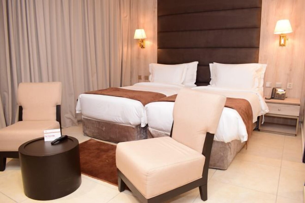 Une chambre d’hôtel avec un lit double, deux tables de chevet, une chaise, une petite table ronde et une lampe.