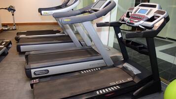 Una hilera de cintas de correr en un gimnasio, con pantalla digital y panel de control.