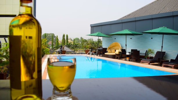 A poolside area with lounge chairs and umbrellas, a bottle of wine, and a glass of wine on a table. - Monty Suites & Golf (Uyo)