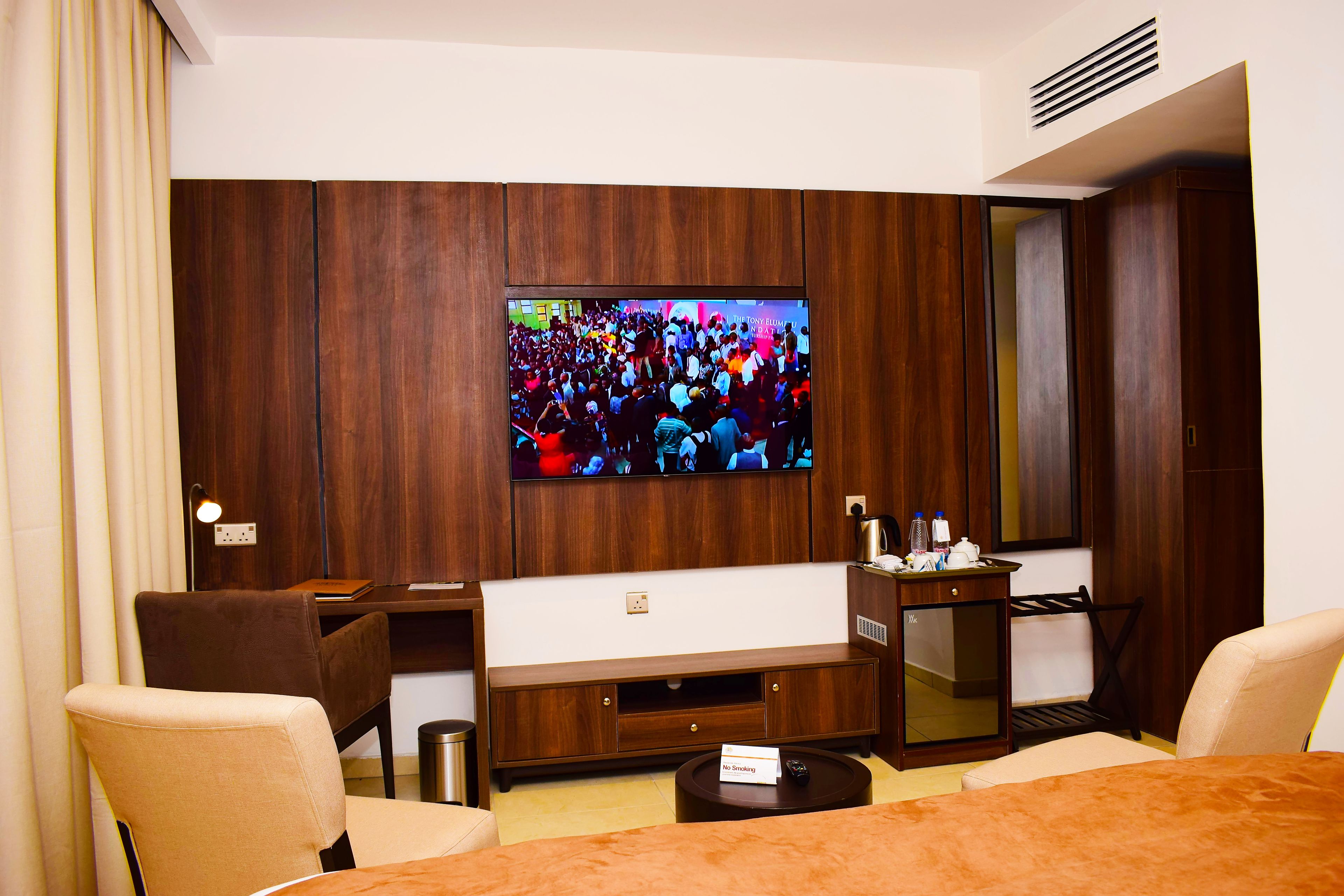 A hotel room with a flat-screen TV mounted on the wall, a sofa, a small table, and a chair.