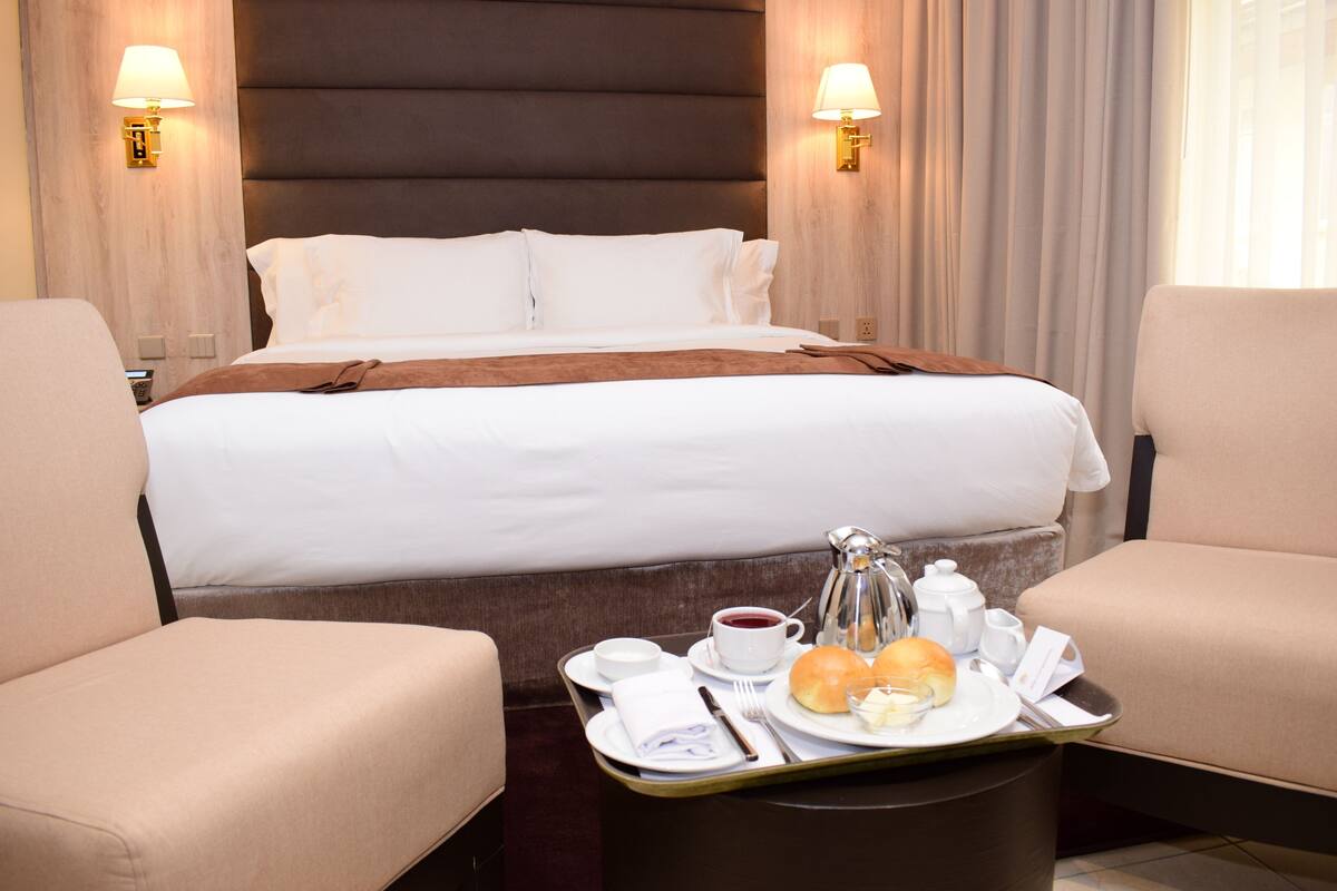 Quarto de hotel com uma cama grande, duas poltronas, um tabuleiro com itens de café da manhã e luminárias fixadas na parede.