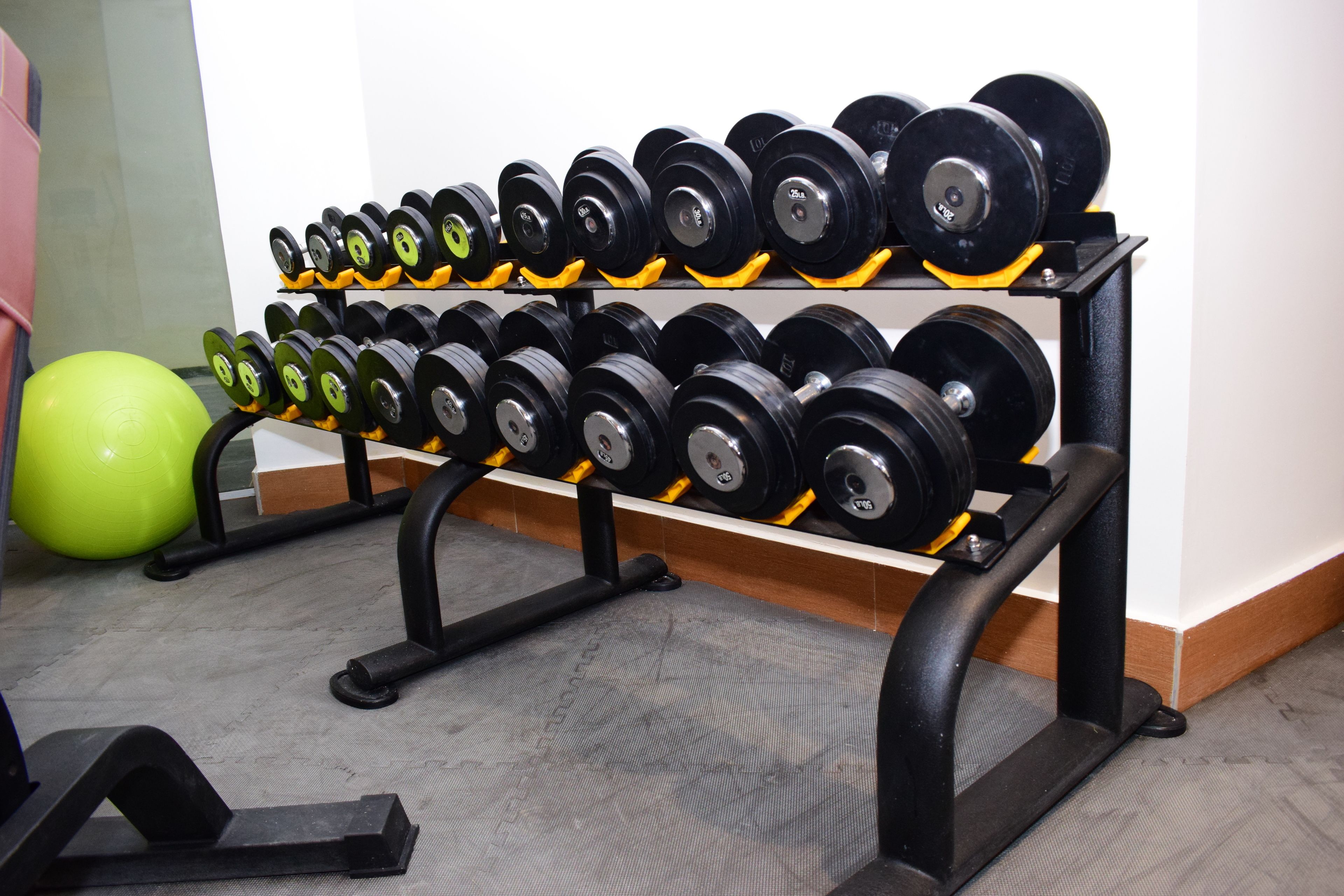 A gym with a rack of dumbbells and a green exercise ball.