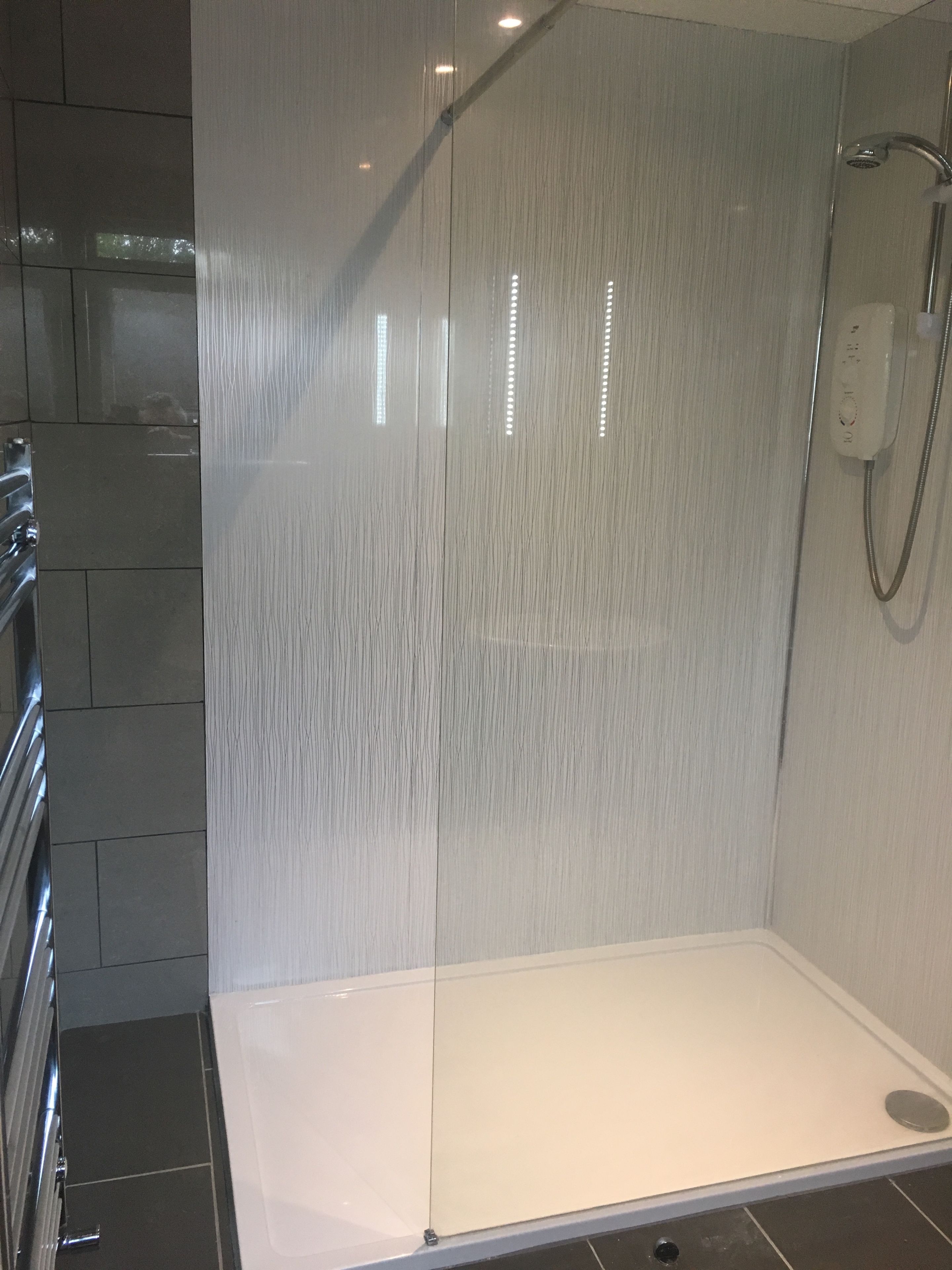 A modern shower area with a glass partition, a white bathtub, and a chrome showerhead.