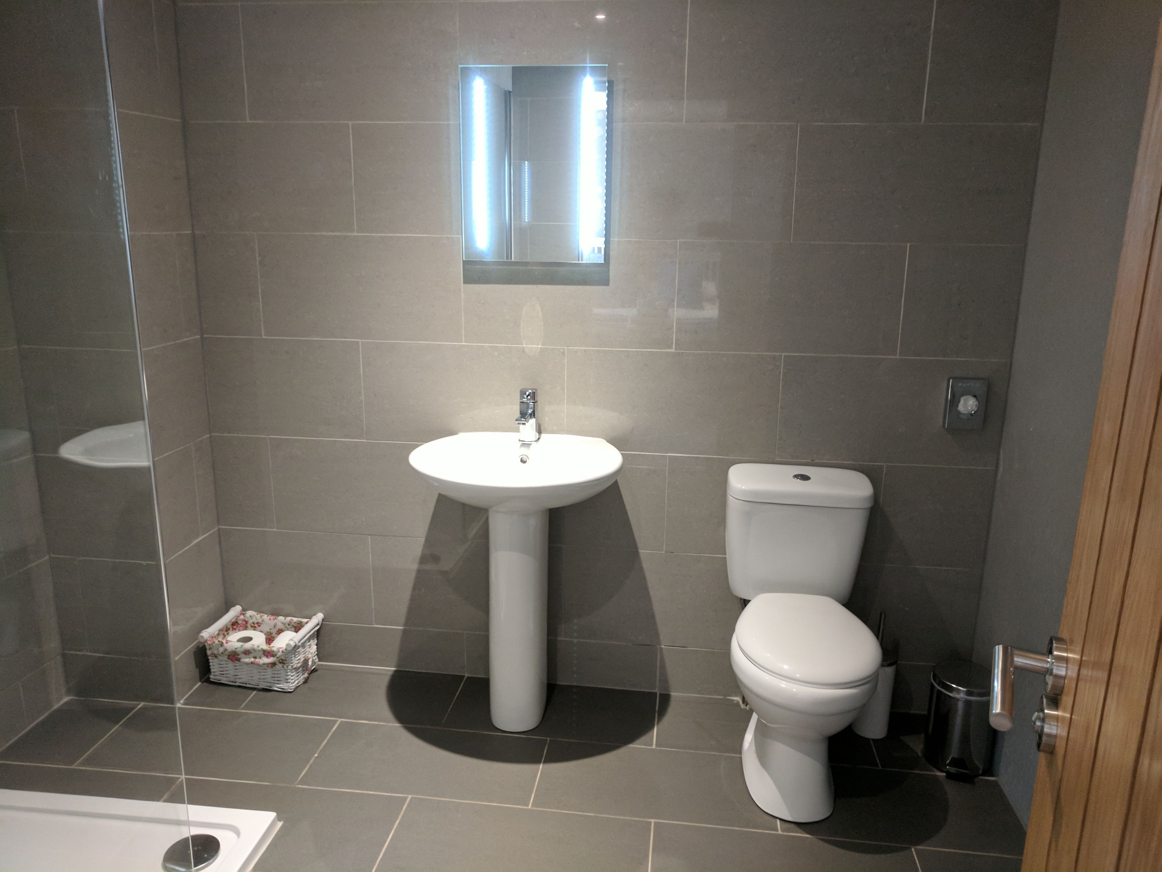 A modern bathroom with a pedestal sink, toilet, and a small mirror above the sink.