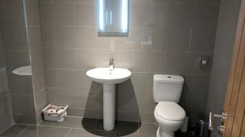 A modern bathroom with a pedestal sink, toilet, and a small mirror above the sink.