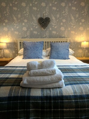 A neatly made bed with a plaid bedspread, two pillows, and a stack of white towels.