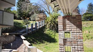Una construcción de ladrillo con un ventanal pequeño, una terraza de madera y una barandilla metálica.