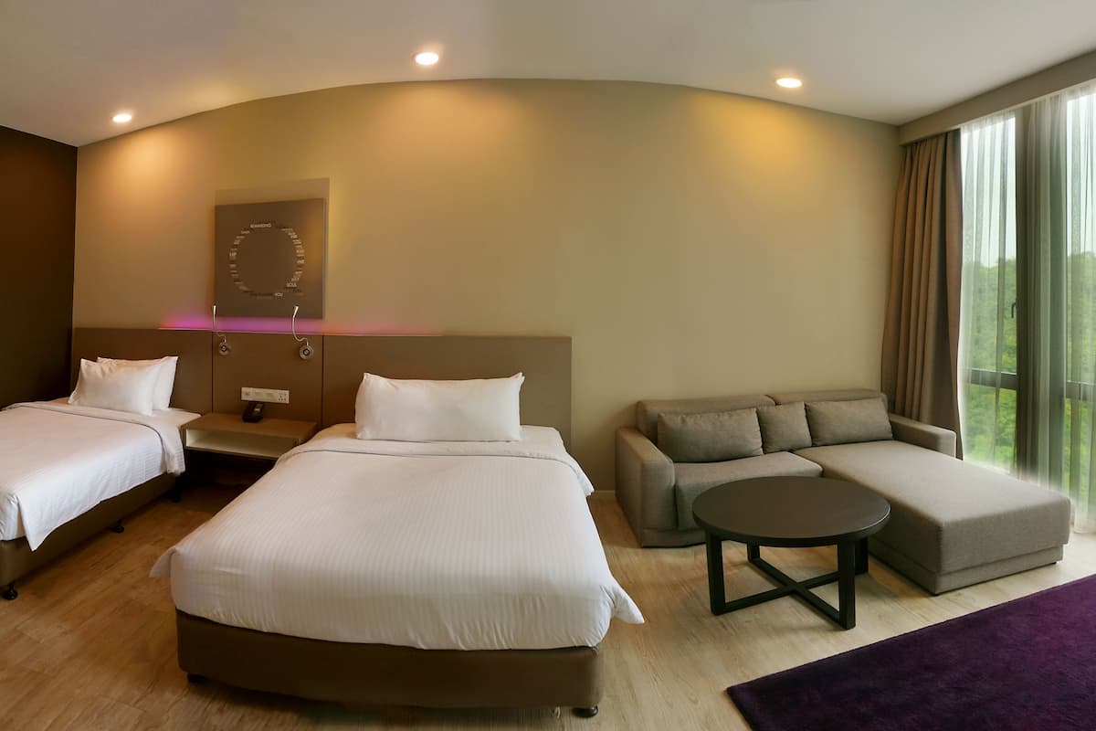 A hotel room with two beds, a sofa, a small table, and a large window offering a view of greenery.