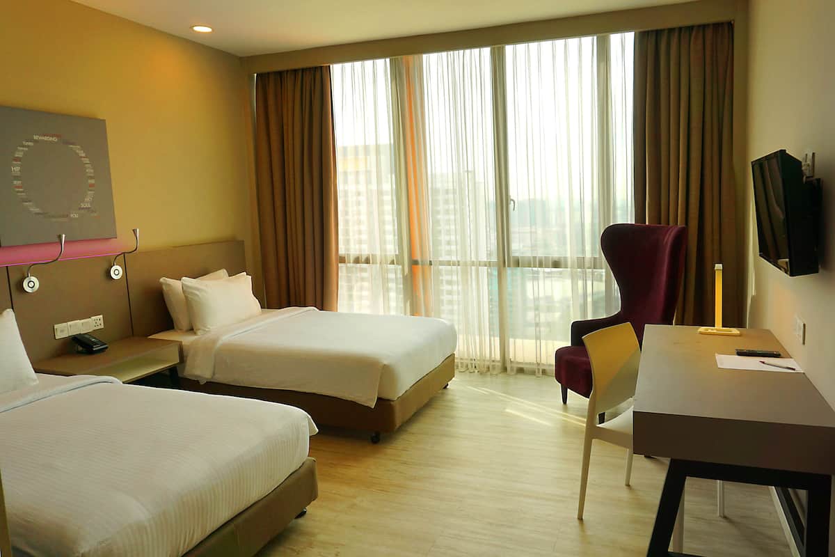 A hotel room with two beds, a desk, a chair, a TV, and a window with curtains.