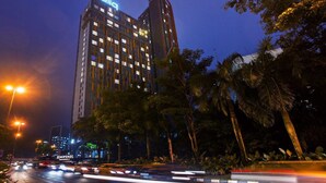 A high-rise hotel with a prominent 'Qdia' sign at the top, surrounded by palm trees and streetlights. - Q Stay at Hotel Damansara (Petaling Jaya)