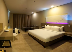 A hotel room with a bed, a desk, a chair, a sofa, and a wall-mounted TV.
