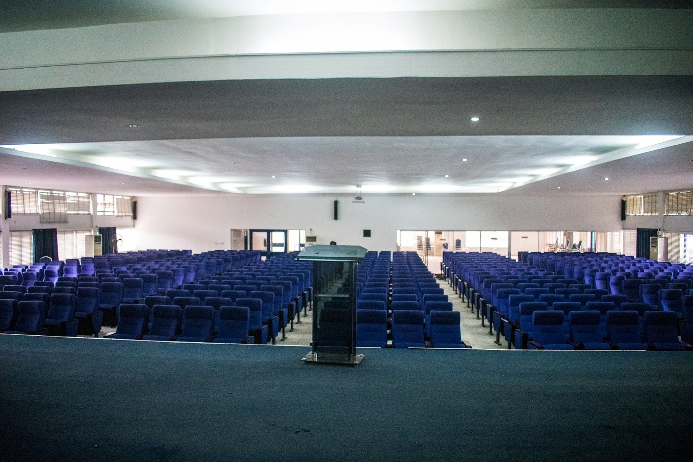 Un salón amplio con filas de sillas azules y un atril en el centro.