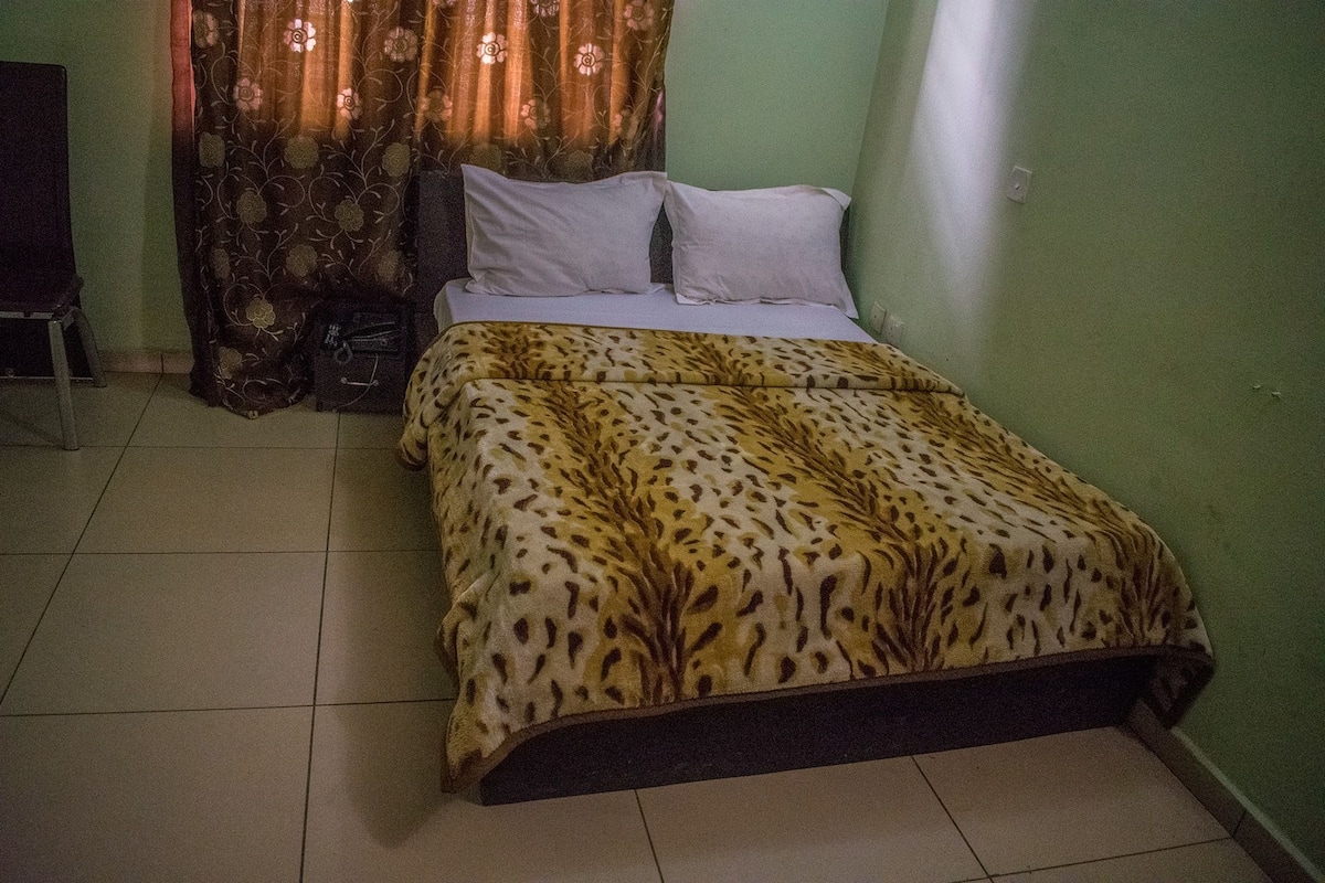A bed with a leopard print bedspread, a chair, and a curtain with a floral pattern.