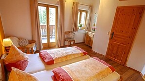 Une chambre avec deux lits, une armoire en bois, un petit bureau avec une lampe et une fenêtre avec des rideaux.