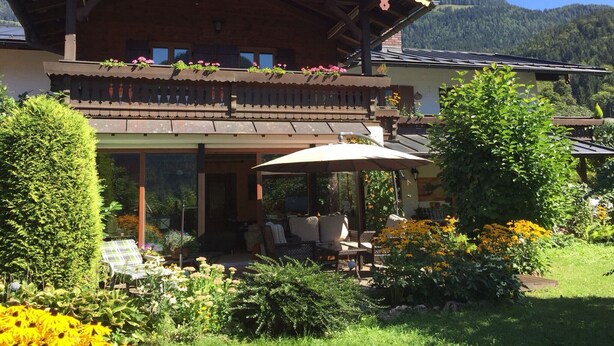 Un bâtiment à deux étages doté d’un balcon, entouré d’une végétation luxuriante et avec une chaîne de montagnes en arrière-plan.