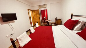 A hotel room with a bed, a TV mounted on the wall, a small table with chairs, and a door leading to a bathroom. - Hotel Drinos (Tirana)