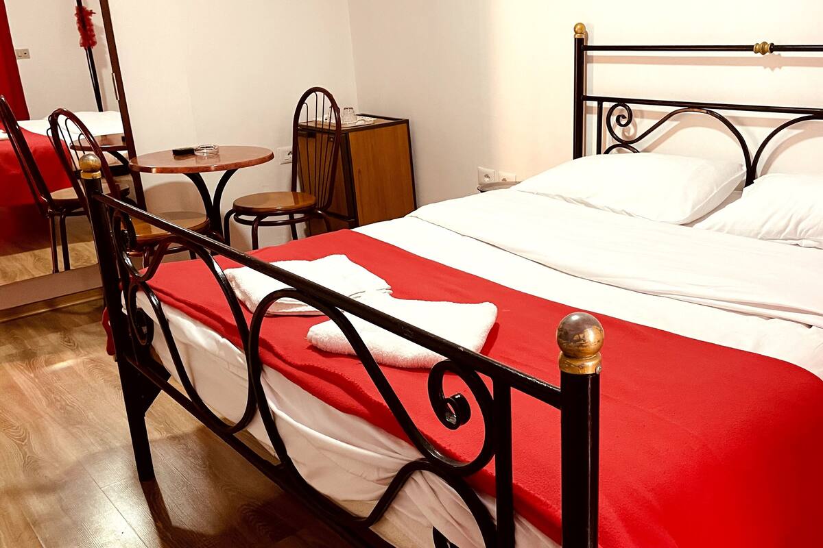 A neatly made bed with a red and white bedspread, a wooden nightstand with a lamp, and a chair in a hotel room.