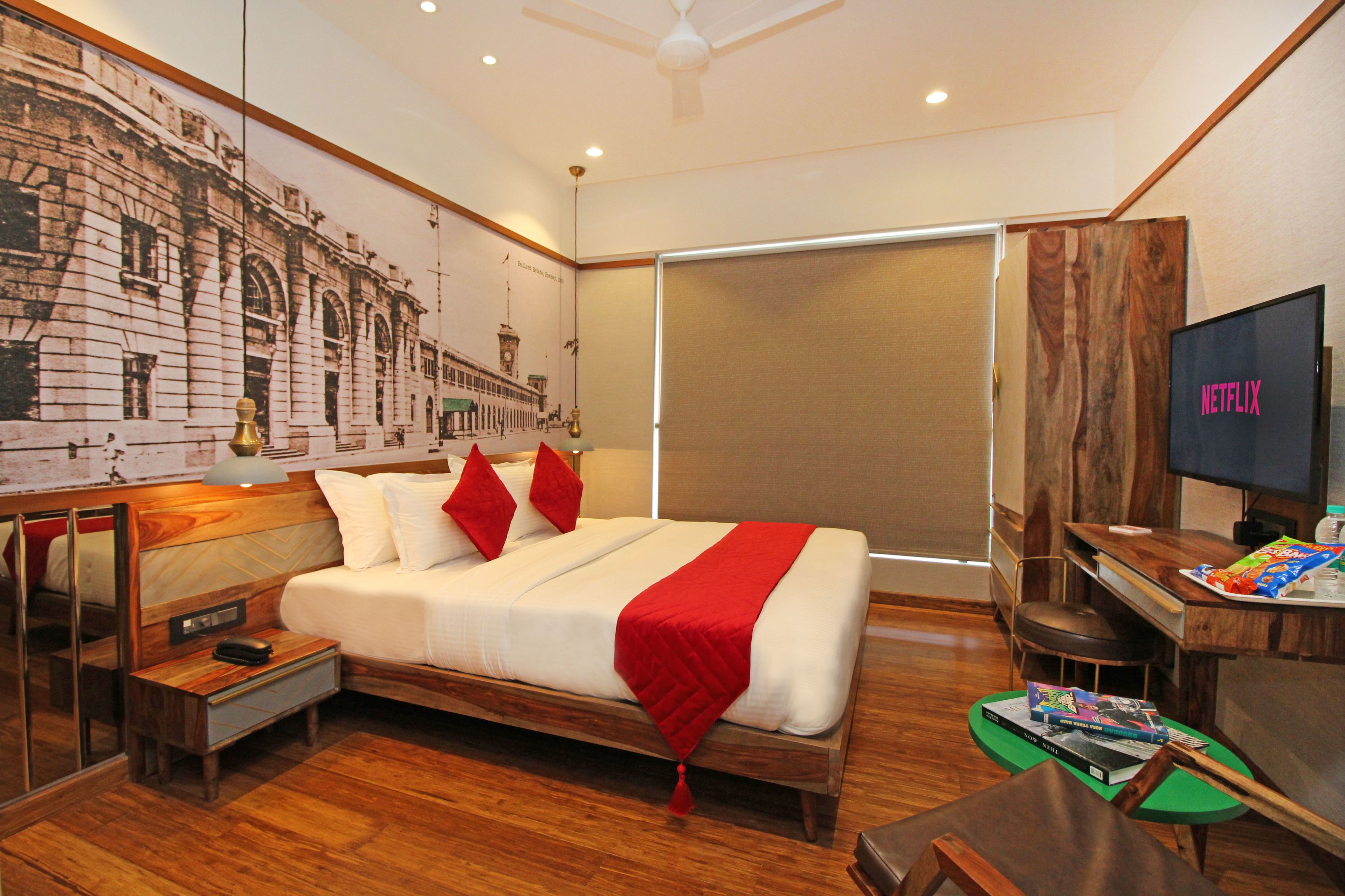 Una habitación de hotel con una cama grande, un televisor, un escritorio con una bandeja de aperitivos y un mural en la pared.