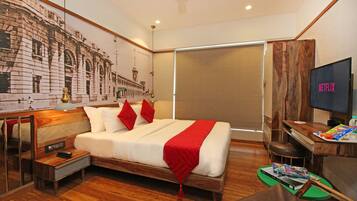 Una habitación de hotel con una cama grande, un televisor, un escritorio con una bandeja de aperitivos y un mural en la pared.