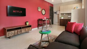A modern living room with a red accent wall, a Netflix sign, a wooden entertainment unit, a green coffee table, and a brown sofa with red cushions. - Theory9 Premium Serviced Apartments Khar (Mumbai)