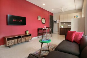 Uma sala de estar moderna com uma parede de destaque vermelha, um letreiro da Netflix, um móvel de entretenimento de madeira, uma mesa de centro verde e um sofá marrom com almofadas vermelhas.