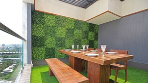 A dining area with a wooden table set for four, a bench, and a green wall. - Theory9 Premium Serviced Apartments Khar (Mumbai)