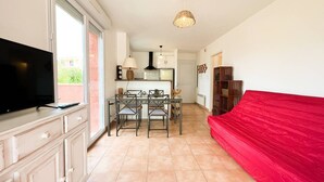 Ein Wohnzimmer mit Fernseher, einem roten Sofa und einem Essbereich mit Stühlen und einem Tisch.