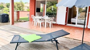 Eine überdachte Terrasse mit Tisch, Stühlen, einem Grill und einer Glasschiebetür, die zu einem Schlafzimmer führt.