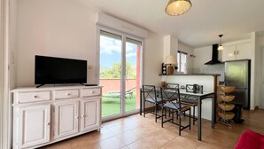Eine moderne Küche mit Essbereich, einem Fernseher auf einem weißen Schrank und einer großen Glasschiebetür nach draußen.